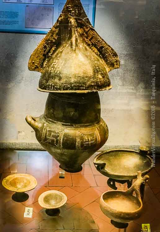 Biconical cinerary urn and various impasto pottery. The single handle or side-loop is typical of the VIllanovan cinerary urns. The crested helmet is decorated with bronze studs. 9th-8th century BCE. National Etruscan Museum - Tarquinia, Italy.